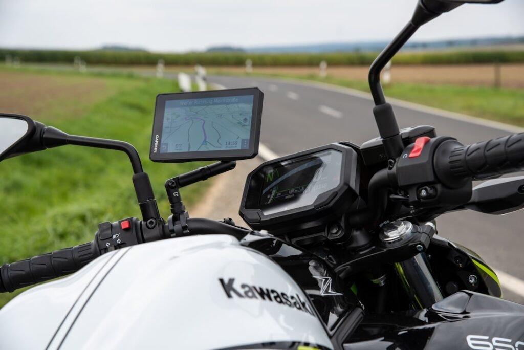 A motorcycle with a GPS device mounted on the handlebars, set against a scenic road view.