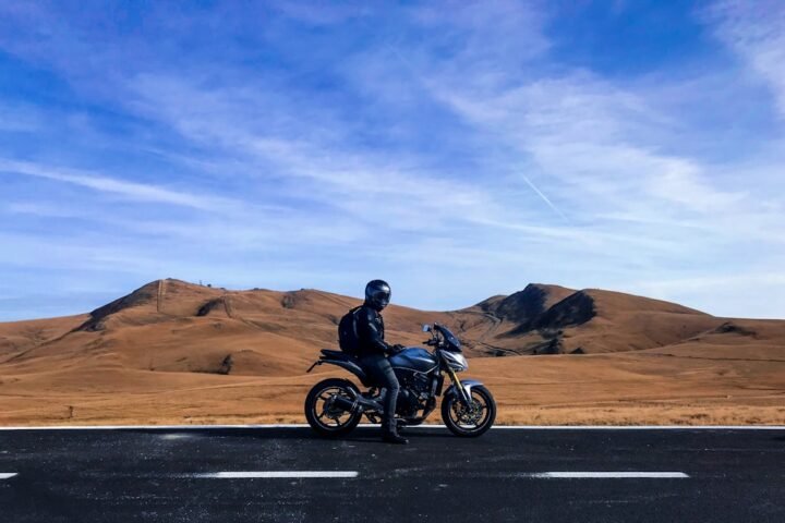 A motorcyclist confidently riding on a scenic road, showcasing a well-prepared bike and a beautiful landscape in the background.