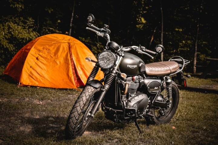 A motorcycle parked near a campsite with camping gear set up, surrounded by nature.