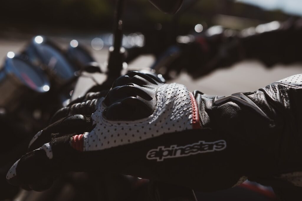 A close-up of a pair of motorcycle gloves on a bike handlebar, showcasing the texture and protective features.