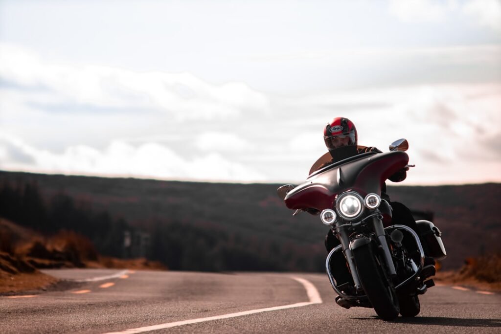 A motorcycle rider wearing a helmet with an intercom system, riding on a scenic road, showcasing communication and connectivity.