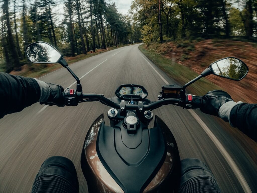 A close-up of motorcycle electrical components including a battery, wiring, and a helmet communication system, set against a blurred background of a motorcycle.
